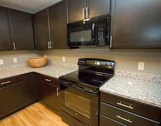 A kitchen with dark brown cabinets, granite countertop, and black microwave and stove