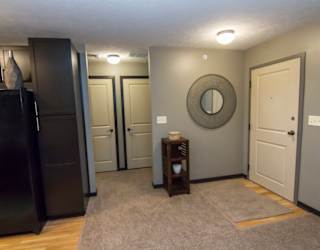 A black refrigerator stands in a kitchen with a grey wall and a round mirror on the wall.