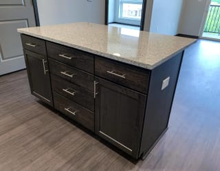 Dark brown kitchen island with light granite counters and storage doors along the front