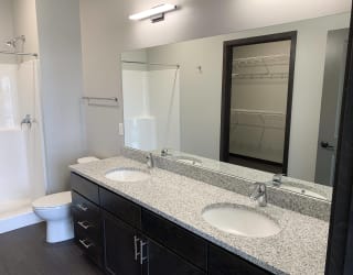 Bathroom with walk in shower, dark brown cabinets and  two sinks in two bedroom apartment at Haven at Uptown