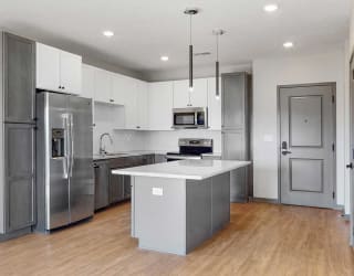 Slate finish kitchen with two tone cabinets, light hard wood style flooring, granite counter tops, and white back splashes in the Bliss floor plan at Haven at Uptown in Lincoln, NE