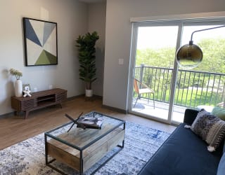 Spacious furnished living room with hard wood style flooring and scenic view of tree line in Lincoln at Haven at Uptown.