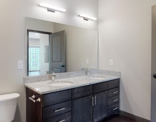 Dual sinks and light granite counter tops, as well is dark wood cabinetry for extra storage in the bathroom at Haven at Uptown in Linooln, NE