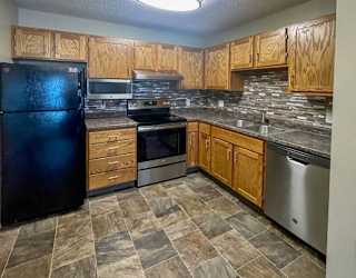 A kitchen with a black refrigerator, wooden cabinets, tile backsplash, stainless steel appliances, and granite countertops.