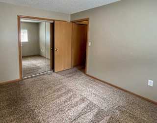 A bedroom with a carpeted floor and closet with a sliding mirrored door.