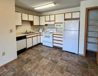 A kitchen with white appliances, a pantry closet, and white cabinets with oak trim.