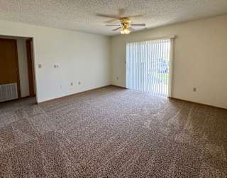 A living room with a ceiling fan, carpeted floor, and sliding glass door to a patio.