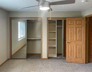 a bedroom with a wooden door, a fan, and two closets with shelves