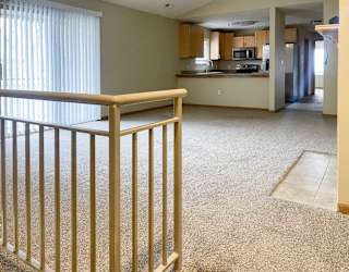 a spacious living area with a carpeted floor and a staircase leading to the entry