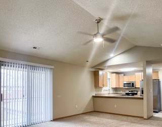 a living room with a sliding glass door to a balcony in front of a kitchen area