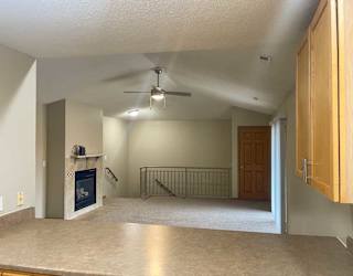 a living room with a fireplace, a ceiling fan, and a metal railing over some stairs