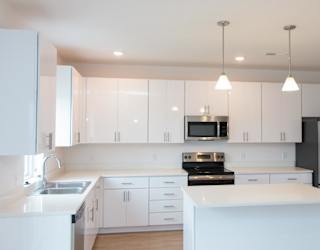 A large L-shaped kitchen with an island. cabinets and counters are white with stainless steel appliances