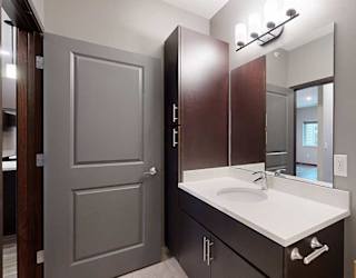 a bathroom with dark storage cabinets, a large vanity sink, and light granite countertops