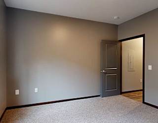a bedroom with carpeted flooring, grey walls, and a large window with a granite windowsill