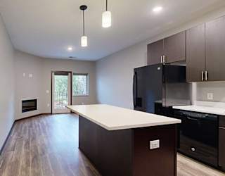 a kitchen island with granite countertop next to a living room and a hallway to the bedroom