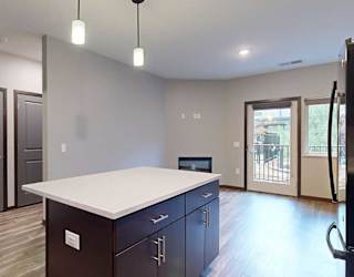 a granite countertop kitchen island in front of a living room and a hallway