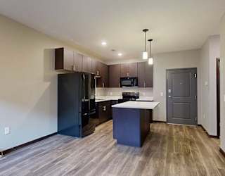 an open-concept living room and kitchen with dark cabinets and black appliances