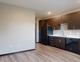 a kitchen with dark wood cabinets next to a living area with hardwood floors