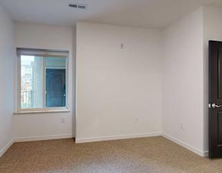 a bedroom with a window looking out to the patio and carpet flooring