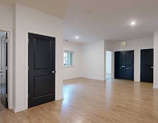 a living room with light walls and dark doors to closets and bedrooms with hardwood floors