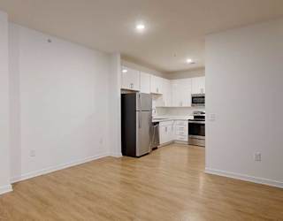 a dining area with hard wood floors in front of a modern kitchen with white cabinets and stainless steel appliances