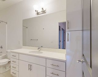 a bathroom with a granite vanity sink, mirror, and white cabinets