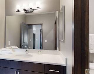 Furnished apartment bathroom with dark finish cabinetry for storage and large mirror