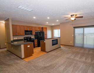 A spacious kitchen with black appliances connected to a carpeted living room