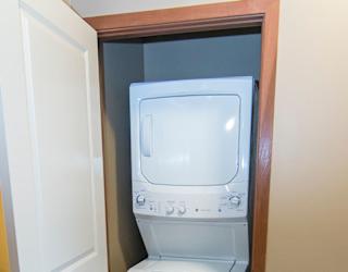 A white washing stacked washer and dryer is in a small closet.