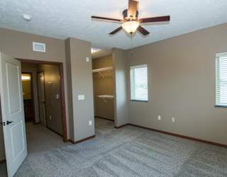 A room with a ceiling fan, open walk in closet, and carpeted floor.