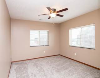 A room with a ceiling fan and two windows.