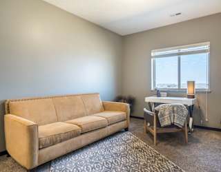 A tan couch sits in a room with a table and chairs.