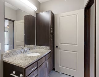 a bathroom vanity with large mirror, light granite countertops, and dark cabinets