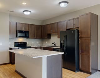 a kitchen with dark cabinets, black appliances, and light granite countertops