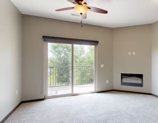 a carpeted living room with an electric fireplace, a ceiling fan, and sliding glass door to a balcony