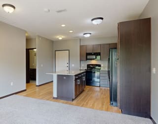 a kitchen with dark cabinets, black appliances, light granite countertops and hardwood flooring