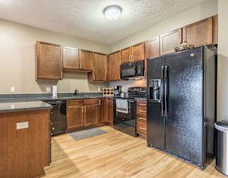 A kitchen with a black refrigerator and warm, medium brown wooden cabinets.