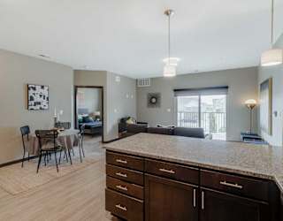 A kitchen with dark wood cabinets and a granite countertop in front of a living room