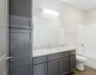a bathroom with a granite countertop sink and a toilet, a tall storage cabinet, and a tub shower