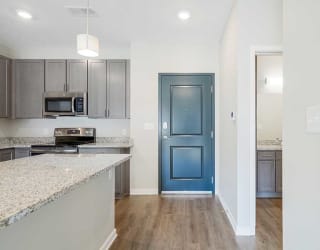 an open-concept kitchen with gray cabinets and stainless steel appliances next to a front door