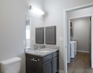 a bathroom with a sink and a mirror across a hallway from a laundry room