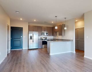 a kitchen with a peninsula, stainless steel appliances, and grey cabinets extending into a living room