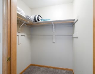 a walk in closet with a white wall and a shelf