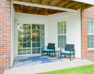 Back patio with two chairs and a rug in front of sliding glass door