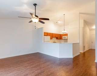 an empty living room with a ceiling fan and a kitchen