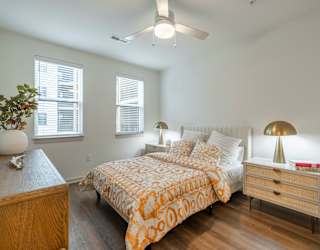 A bedroom with a bed, nightstand, and a plant on a wooden table.