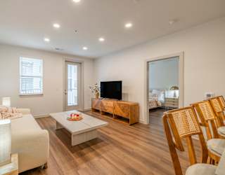 A living room with a white sofa, wooden chairs, and a television.