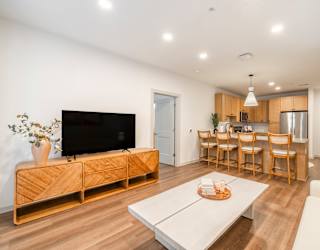 A modern living room with a television, a coffee table, and a dining area.