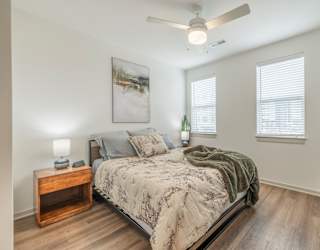 A bedroom with a bed, a nightstand, a ceiling fan, and a painting on the wall.