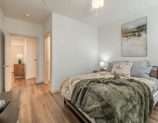 A bedroom with a bed covered in a grey blanket and a painting hanging on the wall.